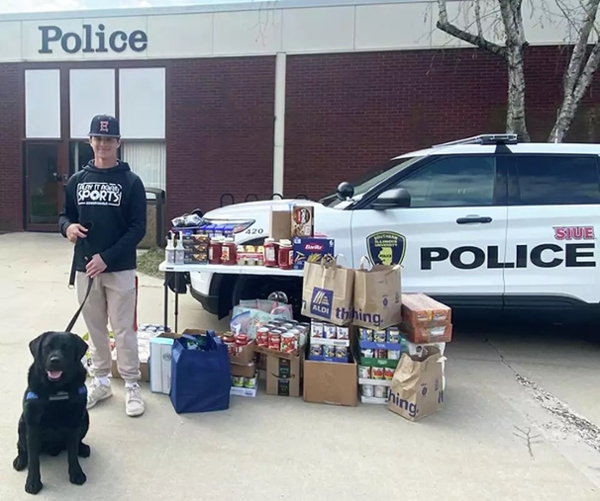Landon and K9 Marshall in front of food donations to Cougar Cupboard